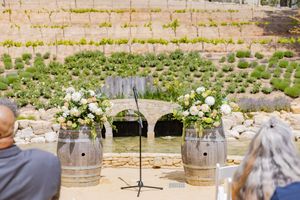 Outdoor wedding ceremony setup with wine barrel pedestals holding white floral arrangements.