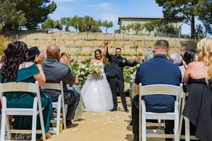 Outdoor wedding ceremony with guests seated in white chairs on a bright sunny day.