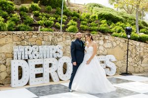 Wedding couple poses by large decorative letters spelling out their names against stone wall.
