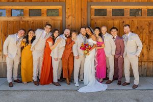 Wedding party in vibrant dresses and light suits poses against rustic wooden barn doors.