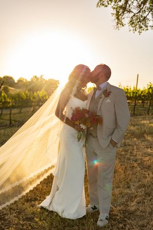 Sunset wedding portrait in vineyard with flowing veil and romantic lighting.