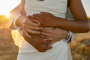 Hands with wedding rings embrace lovingly during golden hour sunset.