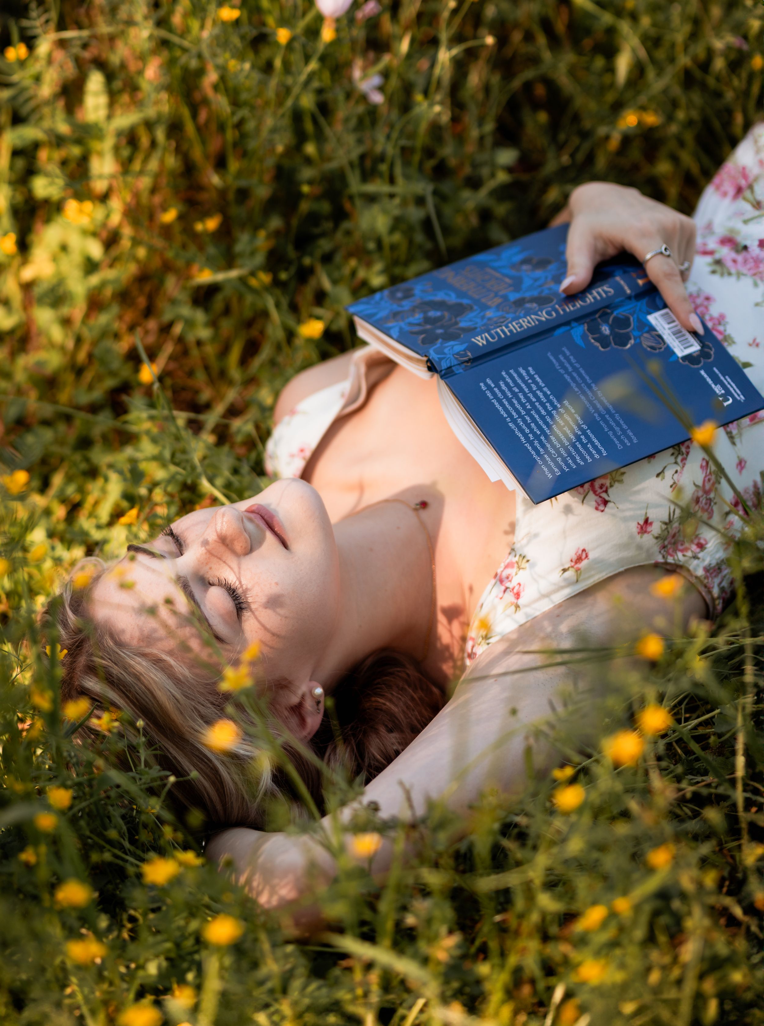 Person lying in field of yellow wildflowers holding a book during golden hour in Spring, Texas.