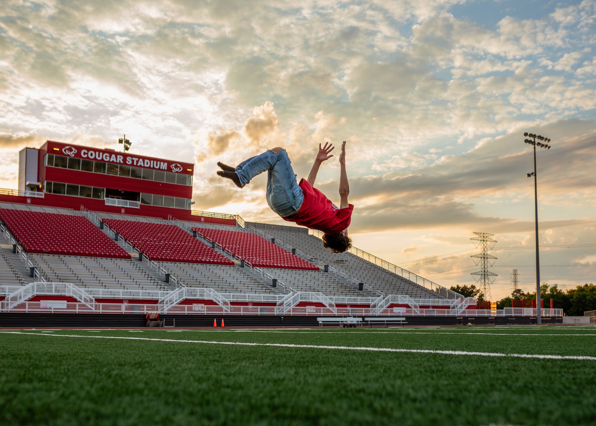 Dramatic sunset over red stadium bleachers with person doing backflip on field in Crosby, Texas.