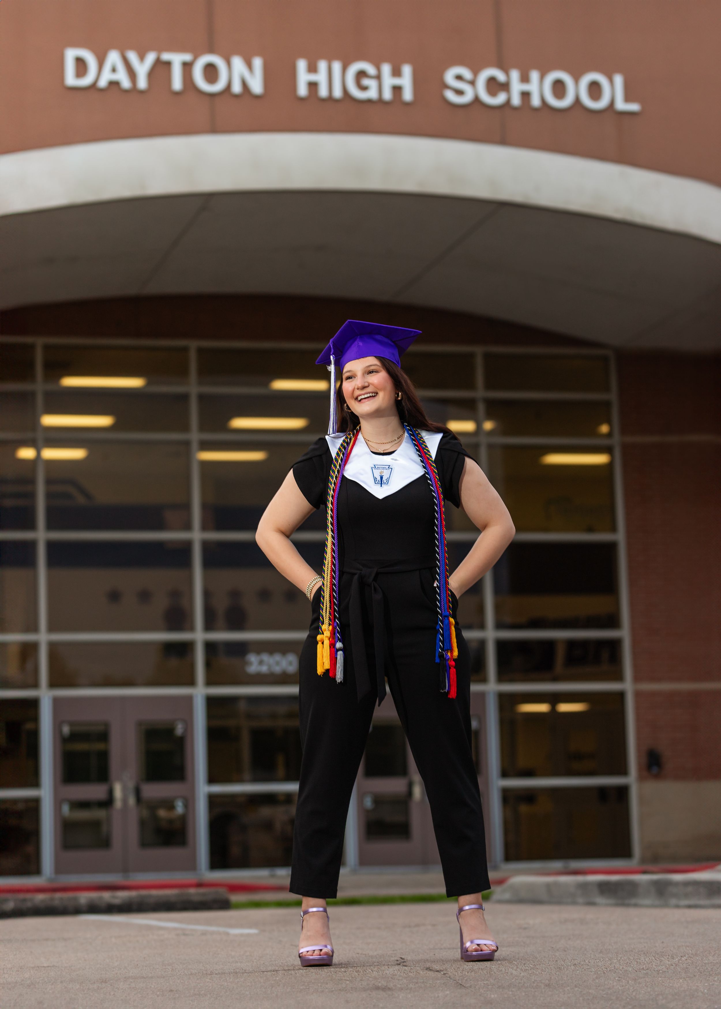 Graduate in cap and gown poses outside Dayton High School entrance.