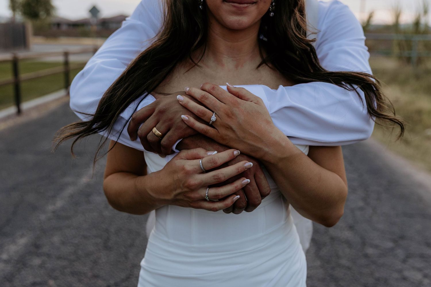 Couple dressed in cozy white sweaters stands in golden field during sunset with beautiful backlighting.
