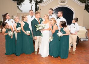 Wedding party in emerald green gowns and khaki suits gather for formal photo on terrace with white floral bouquets.