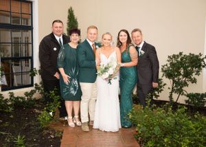 A group in formal attire poses together at a wedding, with attendants wearing emerald green dresses and dark suits.