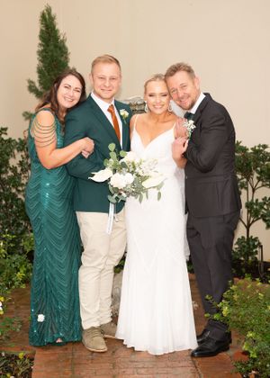 Two couples pose together at an outdoor wedding reception with greenery and brick patio in the background.