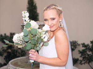 Beautiful bride in a white dress holds a romantic eucalyptus and white floral bouquet while smiling at her wedding.