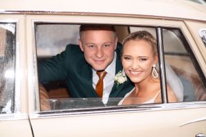 Happy newlyweds smile from inside their classic vintage car during their wedding celebration.