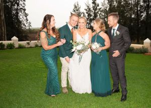 Wedding party in green dresses and formal attire share a candid moment on manicured lawn during outdoor celebration.