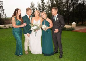 Wedding party in teal and white attire posing together on a lush green lawn at an outdoor venue.