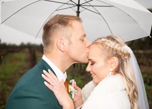 A couple shares an intimate moment under a white umbrella during a wedding photoshoot on an overcast day.