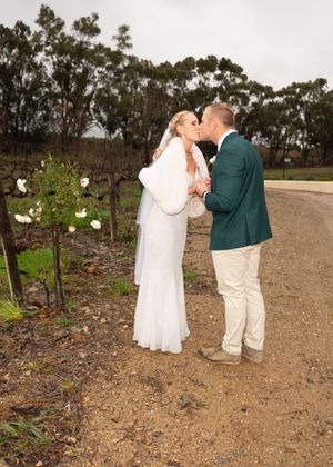 A couple shares an intimate moment together on a dirt path surrounded by trees and flowering vines.