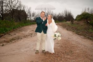 A happy couple poses on a dirt road surrounded by trees while celebrating their special day together.