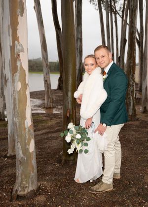 A couple poses romantically among tall eucalyptus trees in a misty forest setting wearing formal winter attire.