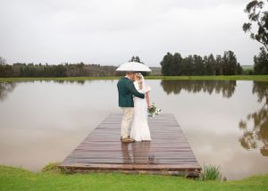 A couple shares a romantic moment under an umbrella on a wooden dock overlooking a serene lake.