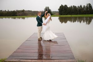 Dancing couple in formal attire celebrate on a wooden dock by a serene lake during an overcast day.
