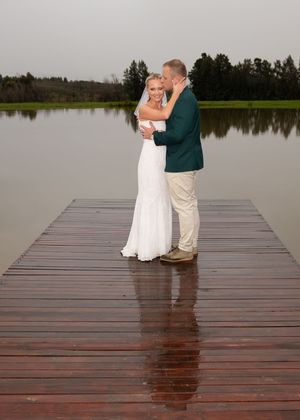 A romantic wedding couple embraces on a wooden dock overlooking a serene lake during an overcast day.