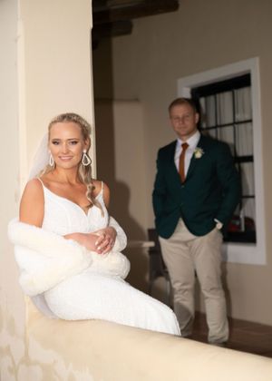 A couple on their wedding day pose in an elegant interior setting with natural lighting and classic decor.