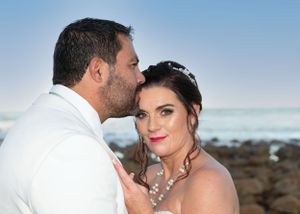 Couple in wedding attire share an intimate moment at a scenic beach location with ocean waves in background.