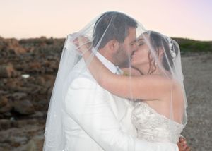 A romantic wedding couple shares a kiss under a flowing veil during their outdoor sunset photoshoot.