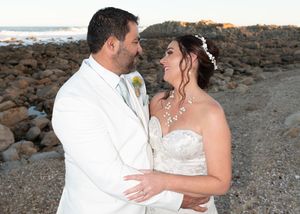 A bride and groom share an intimate moment on a rocky beach during their wedding photoshoot.
