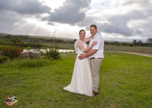 Wedding couple embraces on a grassy hilltop under dramatic cloudy skies during an outdoor ceremony.