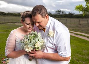 A couple shares an intimate moment on their wedding day while looking at a bouquet of white flowers.