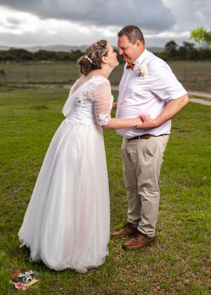 Romantic moment shared between newlyweds on a grassy hill with cloudy skies in the background.