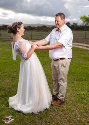 A couple in wedding attire shares a tender moment on a grassy field under dramatic cloudy skies.