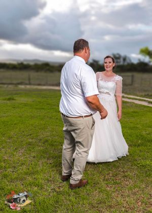 A couple in wedding attire stand on a grassy hilltop under cloudy skies during an outdoor ceremony.