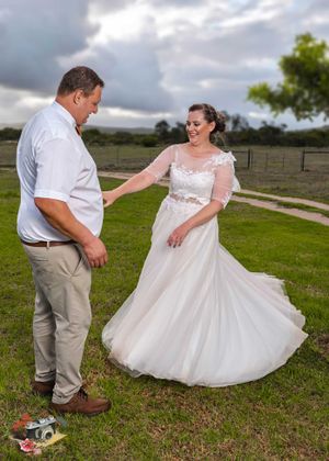 A couple in wedding attire share a joyful moment on grassy grounds under dramatic cloudy skies.