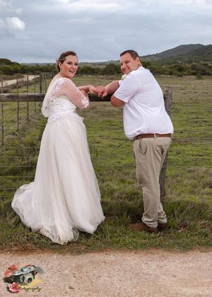 A couple poses on a dirt path with rolling hills in the background during an outdoor wedding photoshoot.