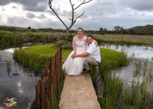 A couple sits together on a pathway surrounded by wetlands and marsh grass under moody storm clouds.