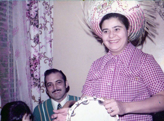 Vintage photograph showing two people at a party, one seated wearing green and one standing in pink gingham with a decorative hat.