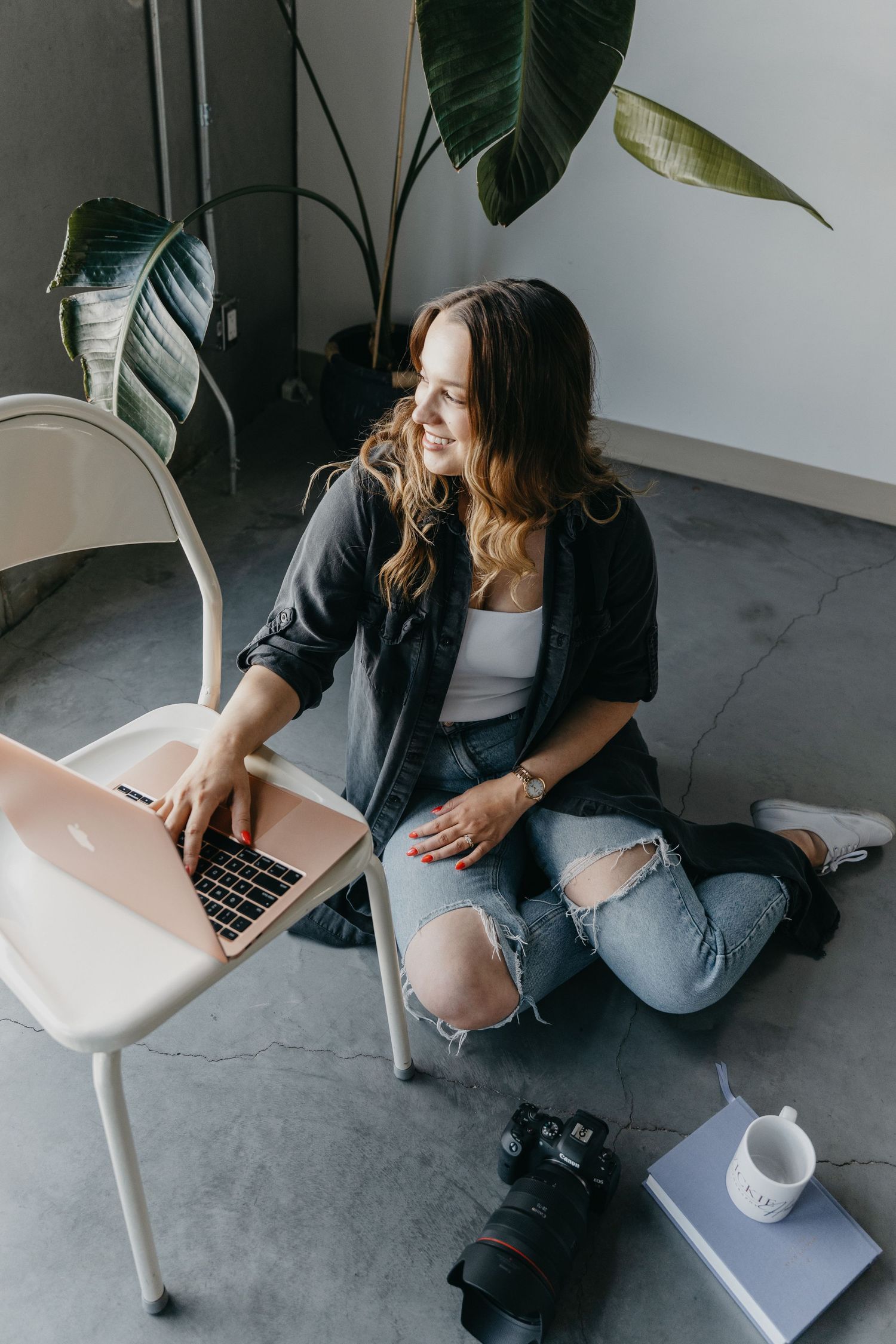 Casual home office setup with laptop, camera and houseplant showing relaxed work environment on floor.