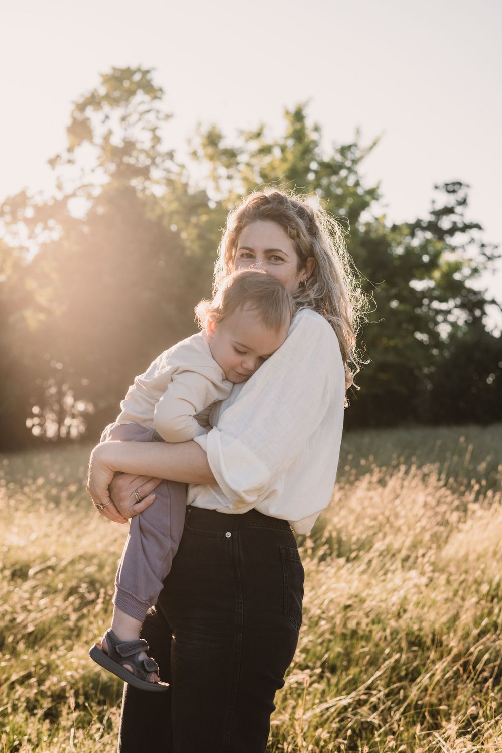 A tender embrace between mother and child in a sunlit field of tall grass at golden hour.