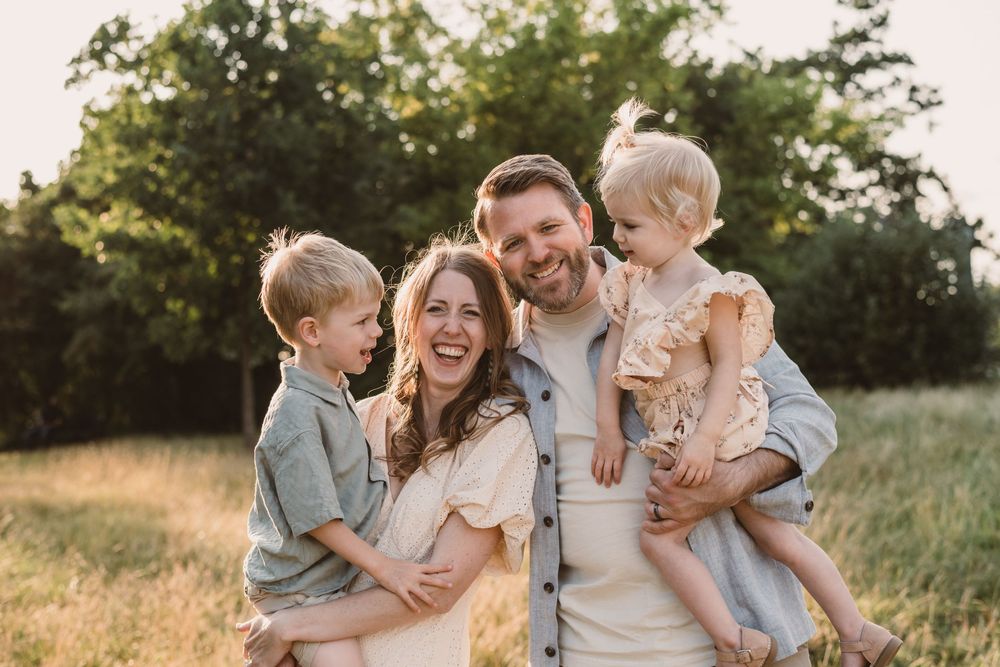 A joyful family embraces and laughs together in a sunlit field during golden hour.