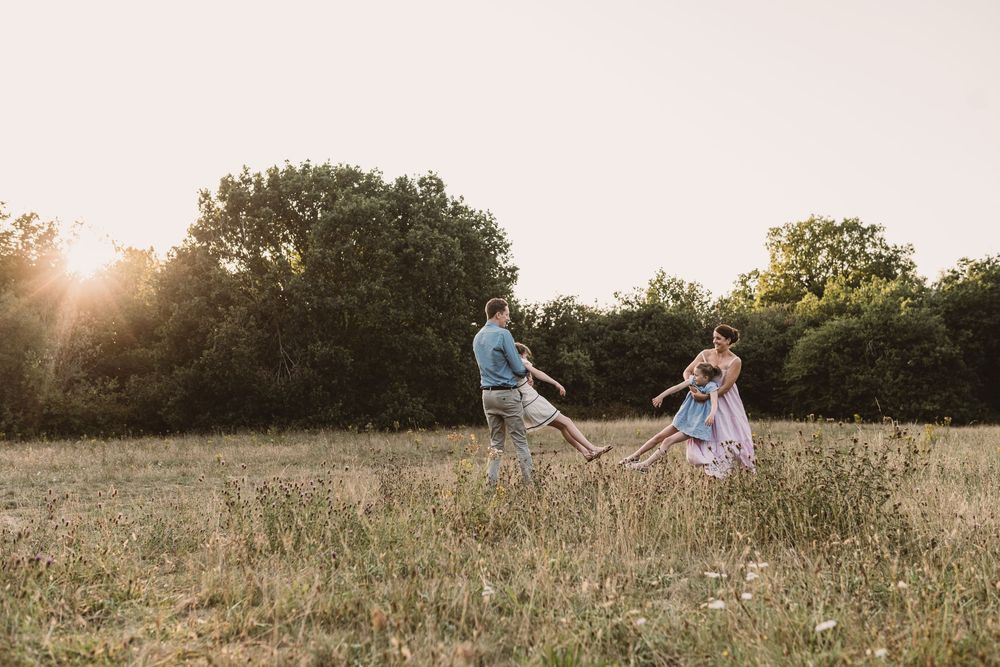 A family having a playful moment in a sunlit meadow at golden hour with trees in the background.