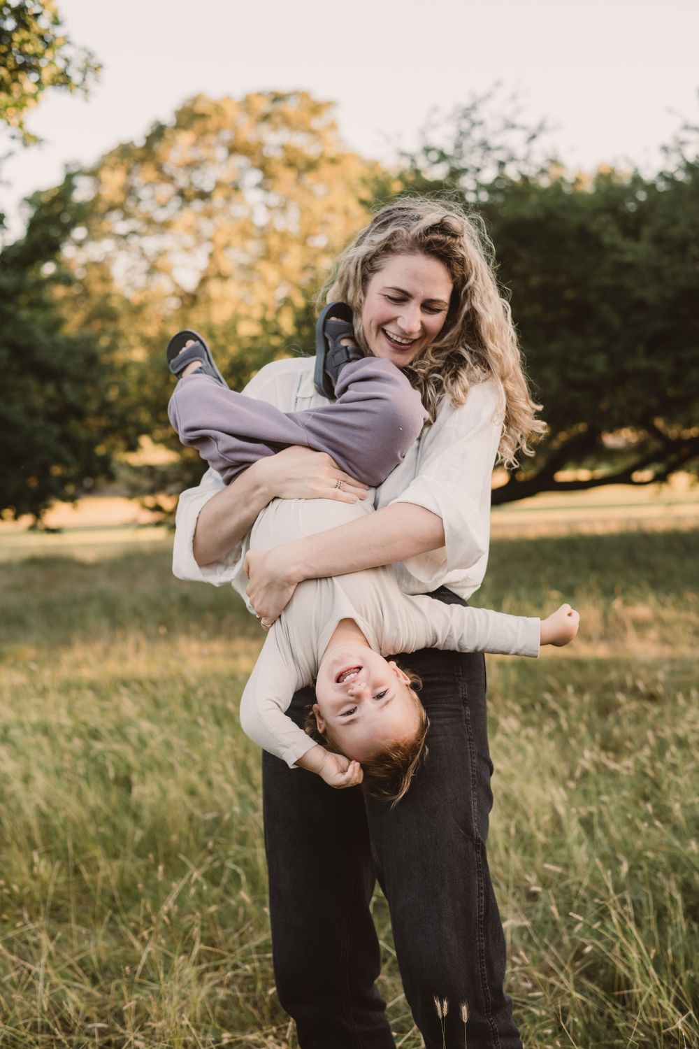 A mother and son play outdoors in tall grass during golden hour.