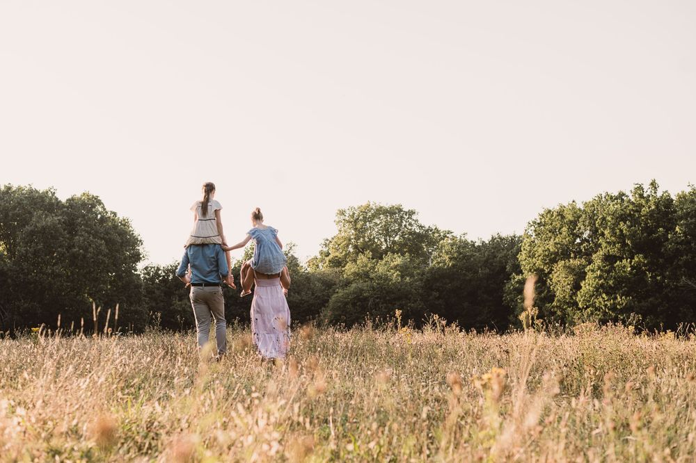 A family walking through a golden summer meadow at sunset as warm light illuminates the tall grass.