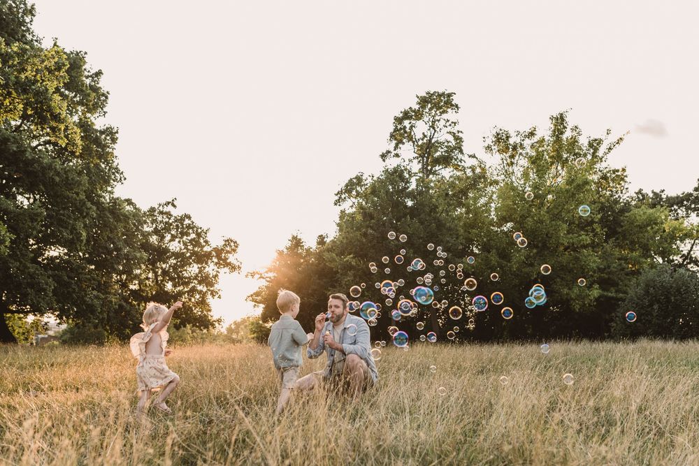 Children playing with soap bubbles in a golden sunlit field at sunset as bubbles float through the air.
