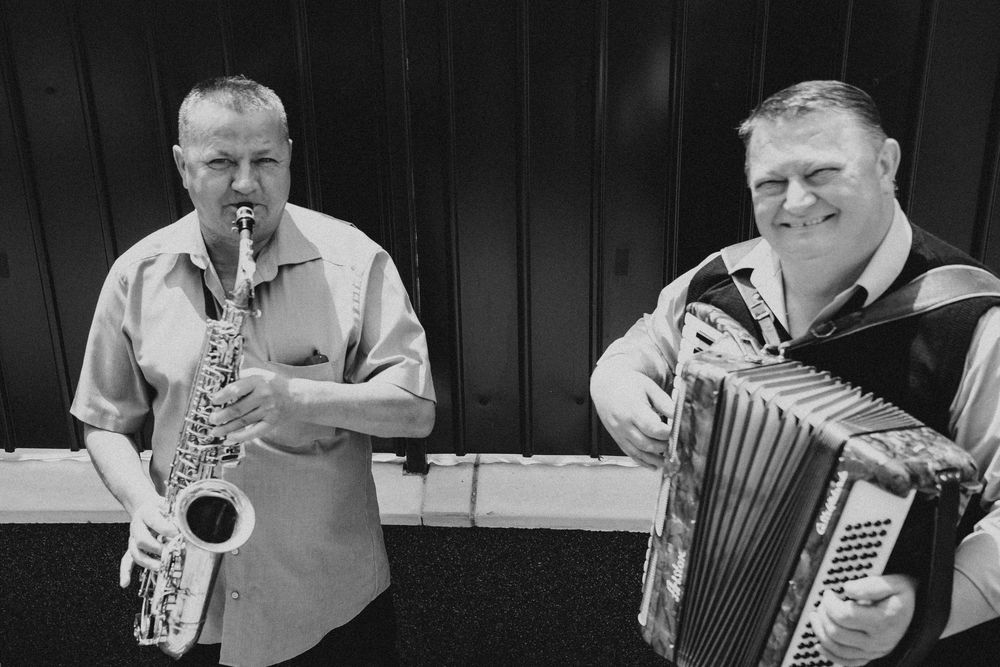 Musicians playing saxophone and accordion perform in black and white photography.