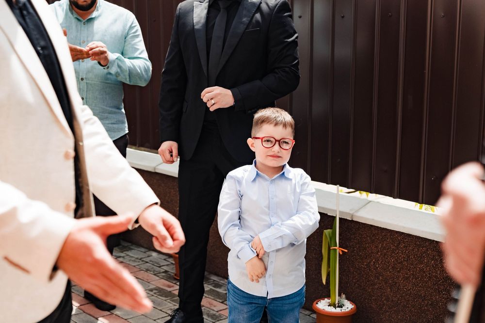 Young boy in formal attire stands among adults during wedding celebration.
