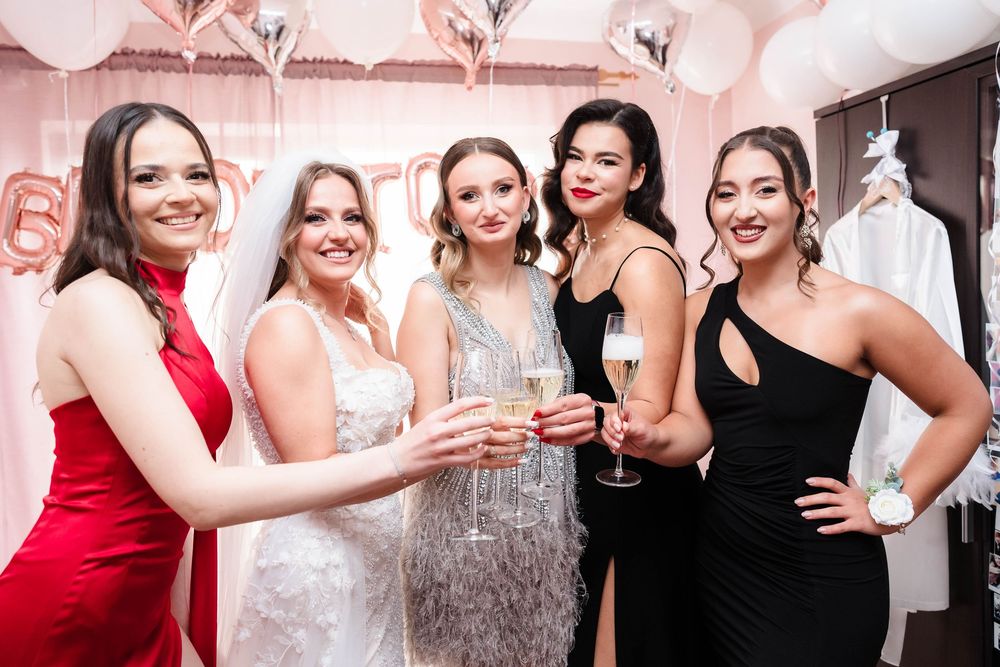 A group of friends in formal dresses celebrate at a bridal party with champagne and smiles.