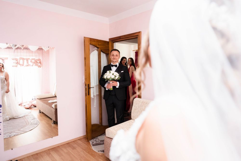 A wedding first look moment captured through a doorway with pink walls and religious artwork.