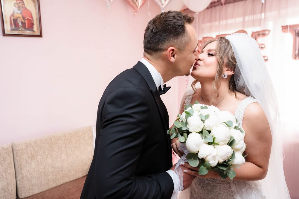 A tender moment between newlyweds with white roses against a pink backdrop.