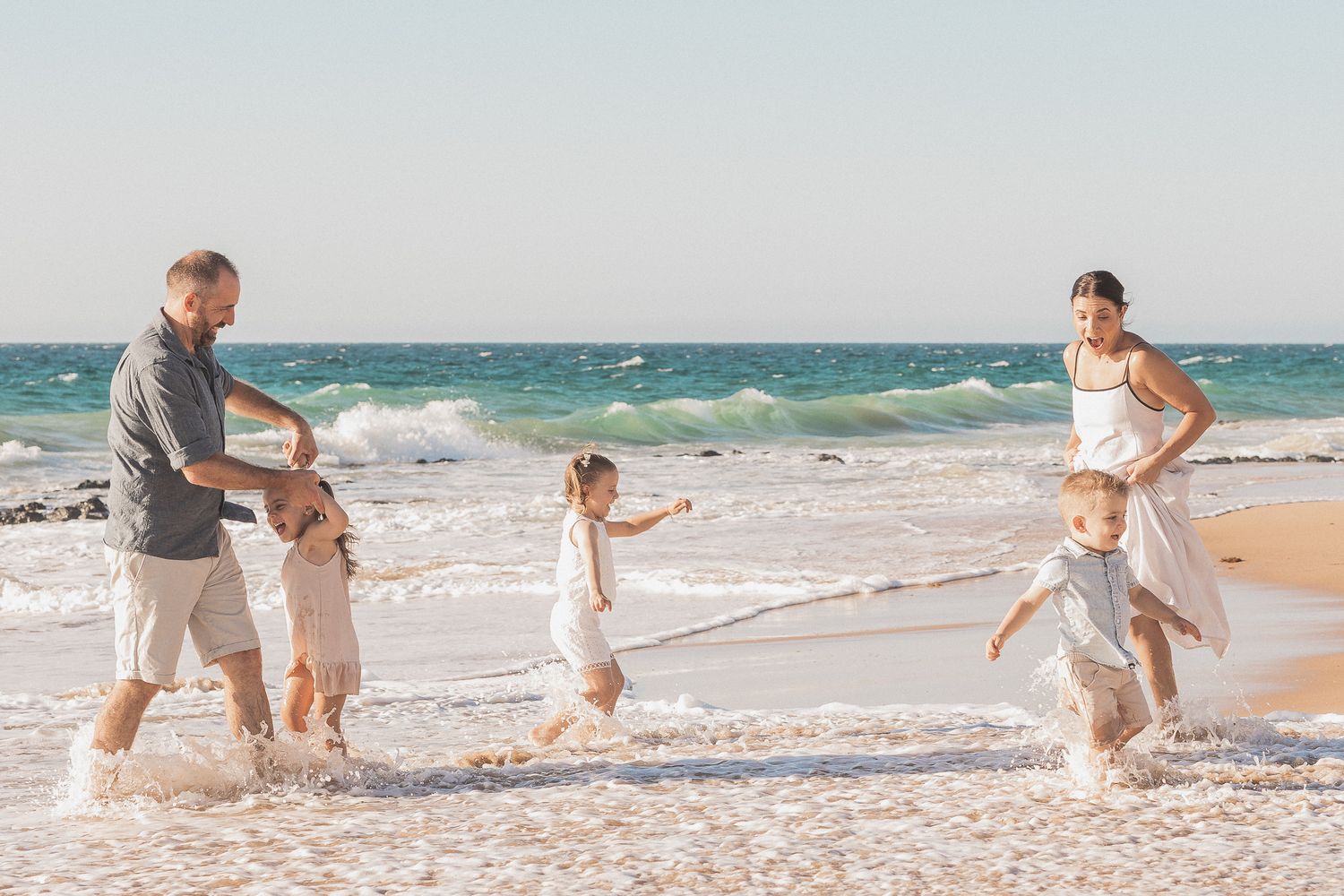 A family plays together in the ocean waves at the beach on a sunny day.